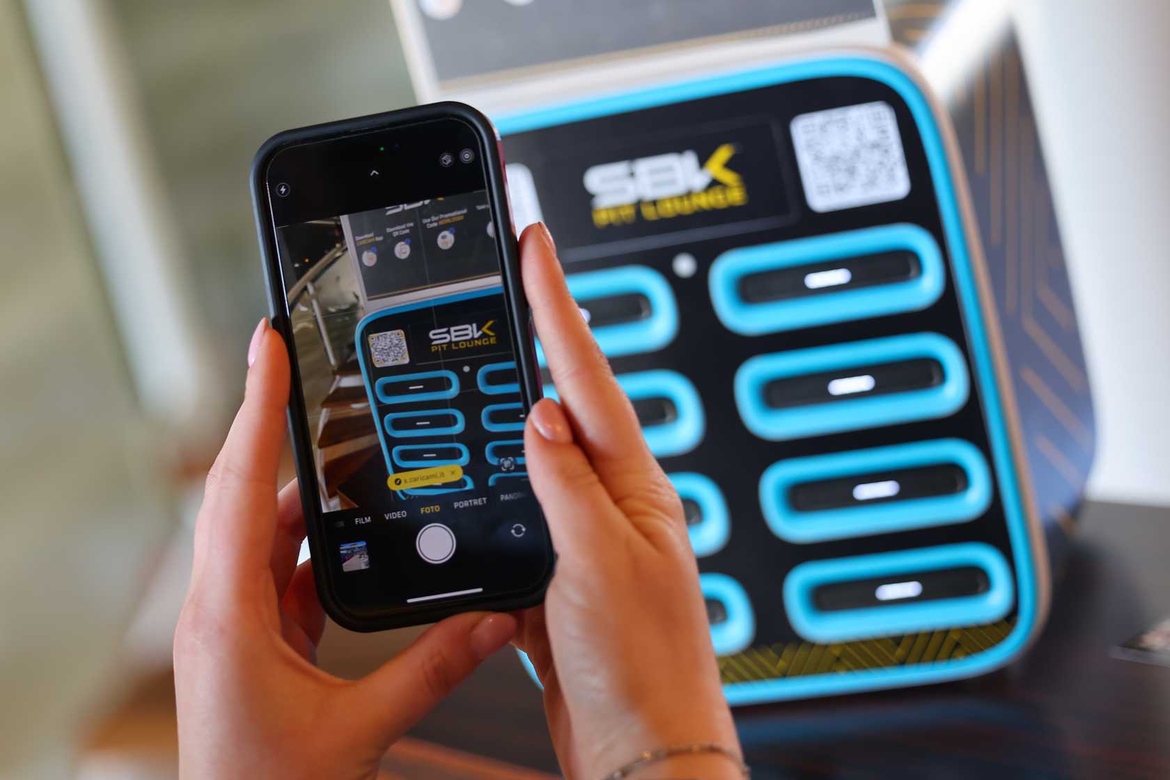Stazione Caricami personalizzata per l'evento WorldSBK con in primo piano telefono che scansiona il QR code per noleggiare un powerbank.